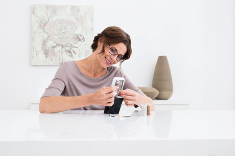 Woman using a Mobilux LED magnifier to aid her in threading a needle.