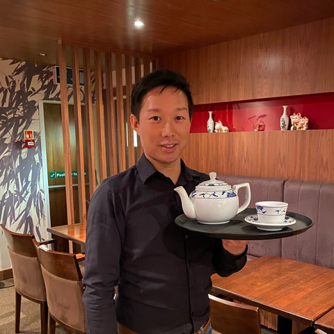 Vincent in his parents' restaurant holding a tray containing a Chinese tea pot and Chinese cup