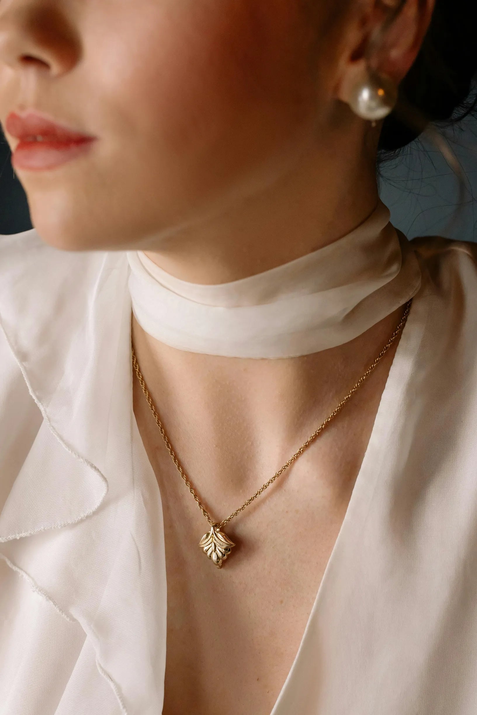 Close-up of a woman wearing a delicate gold pendant and a silk blouse for an elegant look.