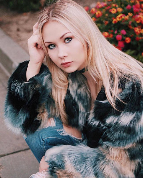 woman staring at camera wearing ripped jeans and faux fur coat