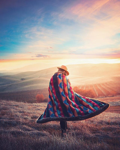 person wearing cowboy hat wrapped in faux fur throw walking through grass