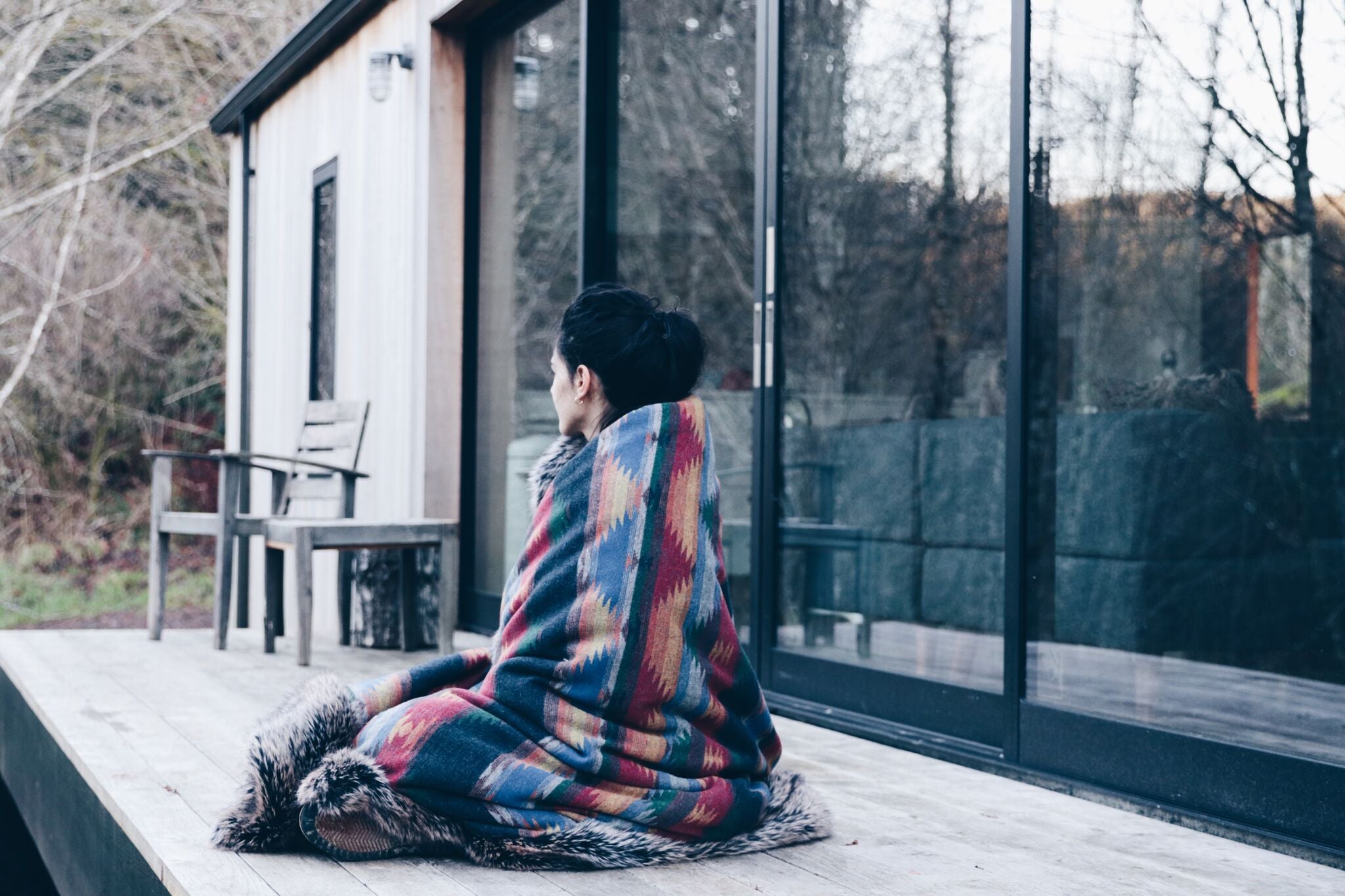 person wrapped in faux fur blanket sitting on deck