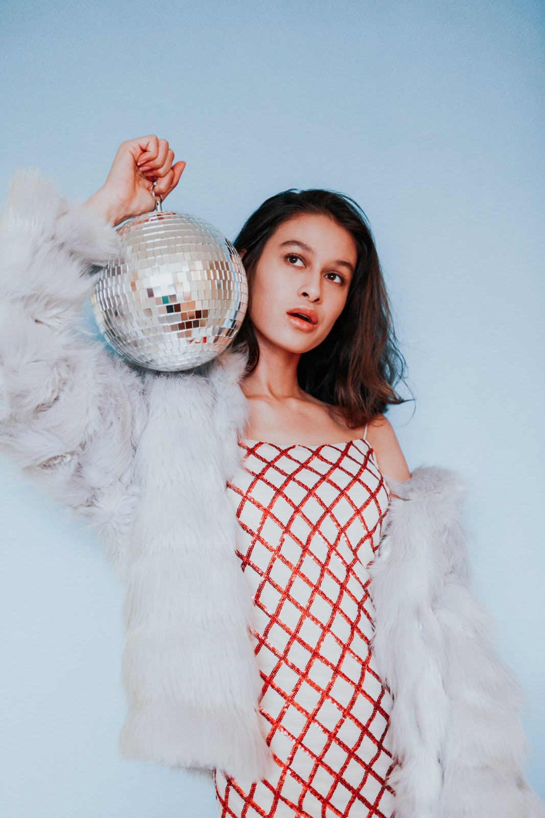 woman holding disco ball wearing faux fur coat and red and white top