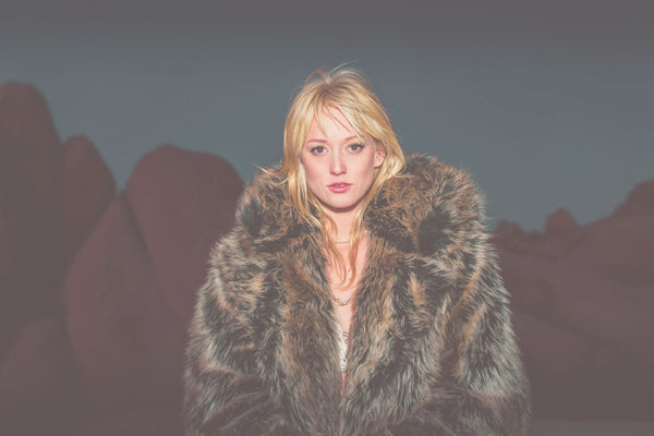 woman wearing faux fur coat with blonde hair staring at camera at nighttime