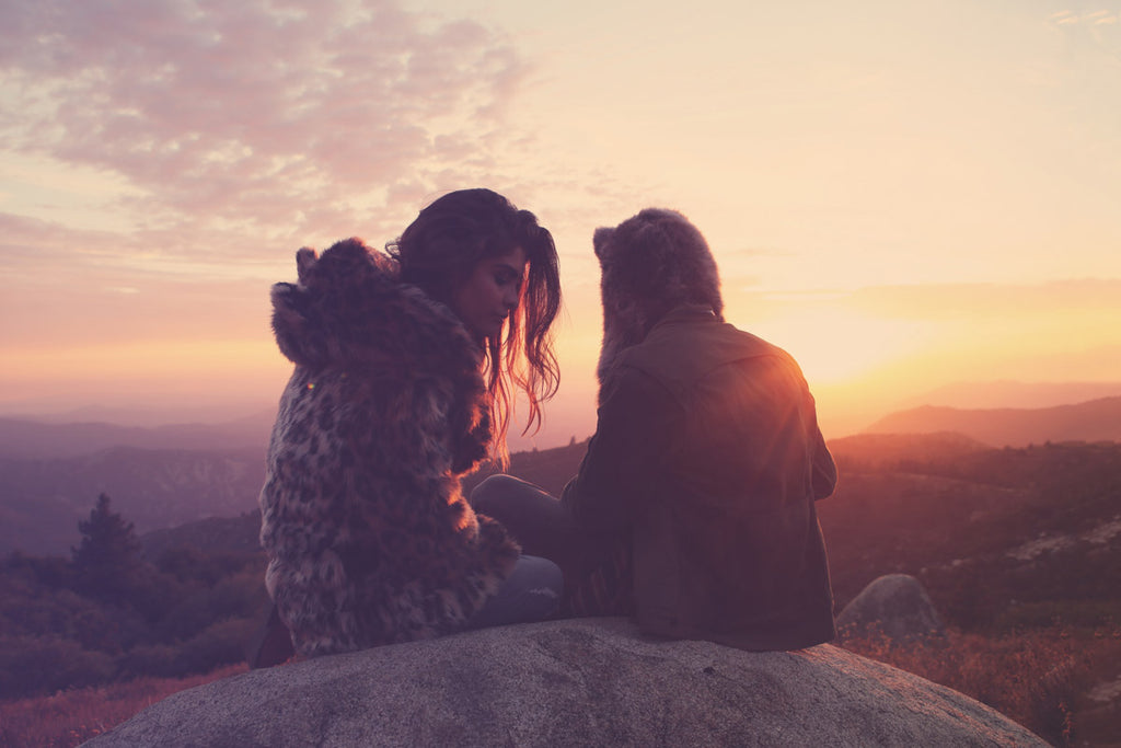 man and woman sitting on rock wearing faux fur at sunset