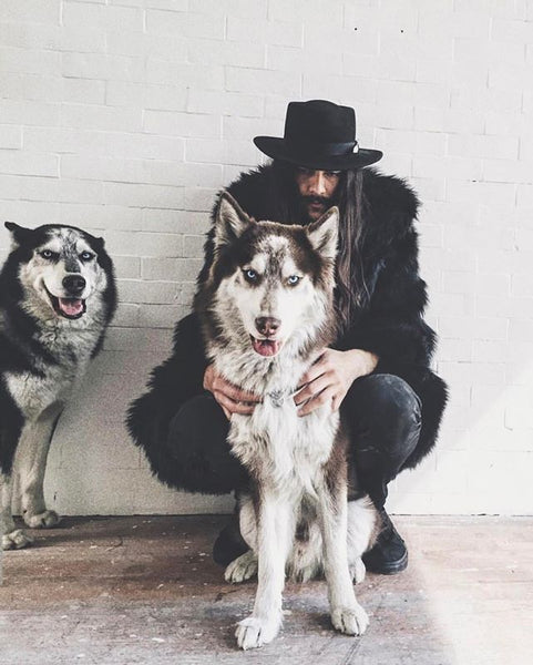 man wearing faux fur coat while petting one husky dog and other husky dog is next to him