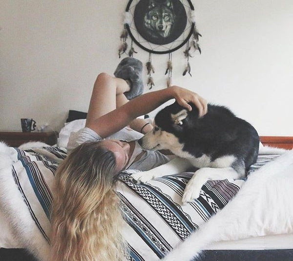 woman lying on bed with huskey dog on top of faux fur throw