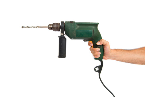 Image of a hand holding up an old green corded drill with a white background.