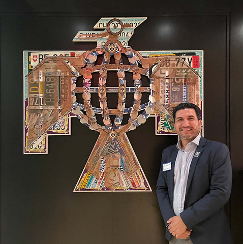 Image of the artist smiling in front a thunderbird made of license plates they created