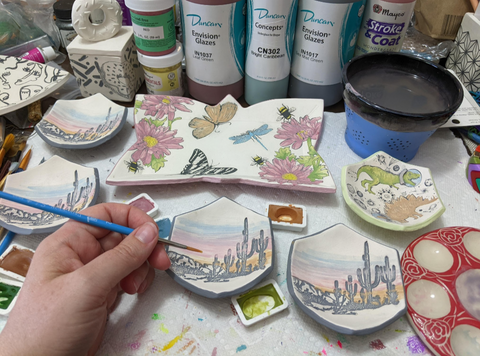 Photo of the artist paining pieces of their ceramics