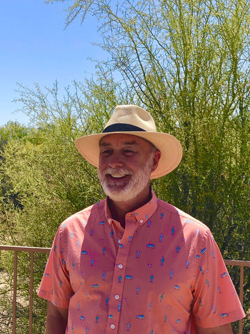 Photo of the artist, Michael Clark, standing outside in front of desert foliage, smiling in a sun hat