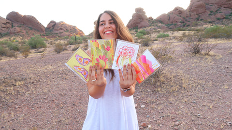 Artist holds out 4 of their cards in front of a desert background