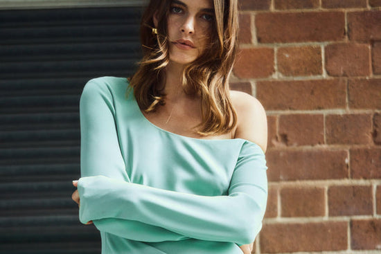 Women leaning against brick wall with arms crossed wearing Mint Dress 