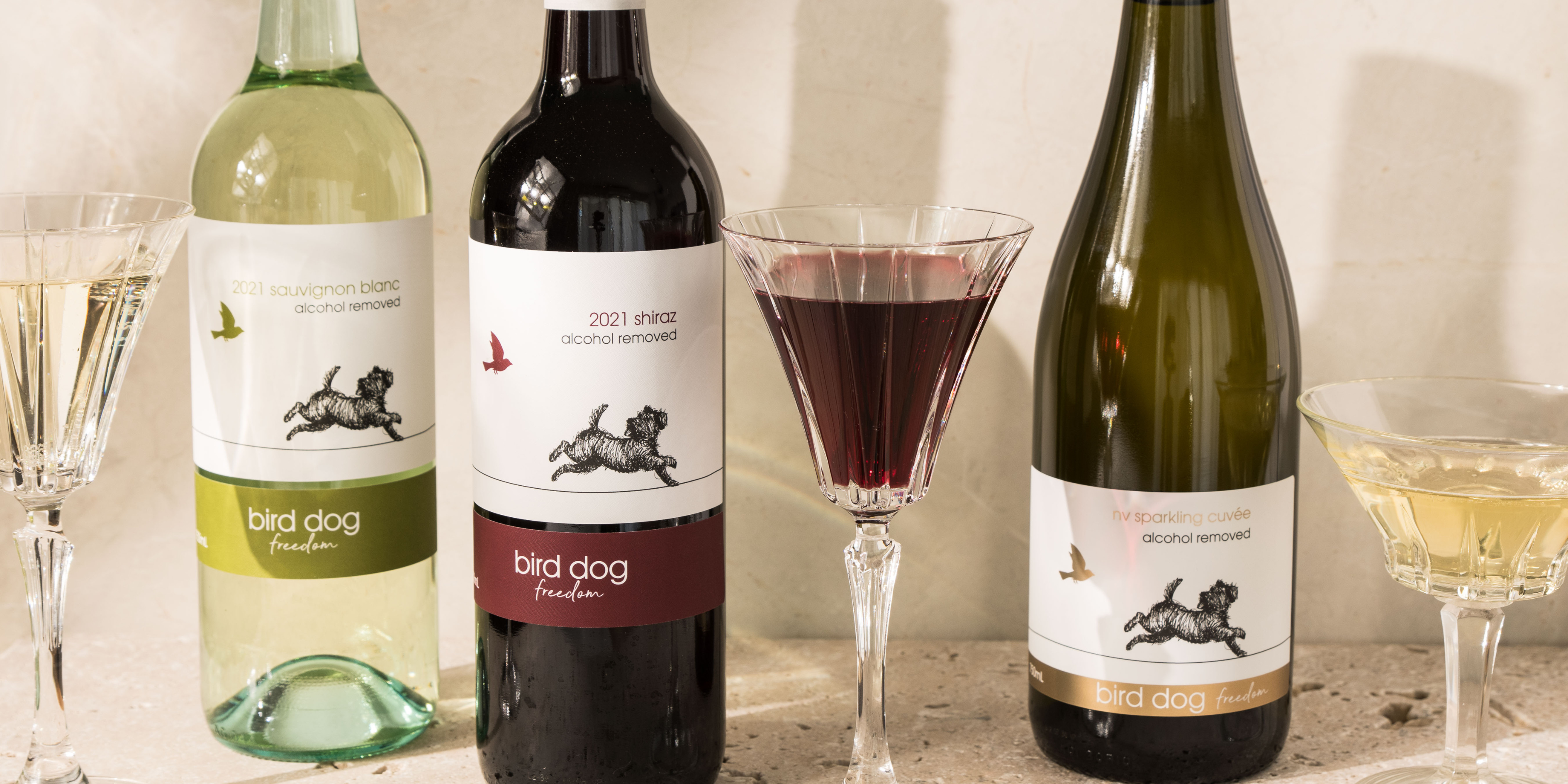 A bottle of each Bird Dog Alcohol removed wine with a poured glass of each beside the bottles