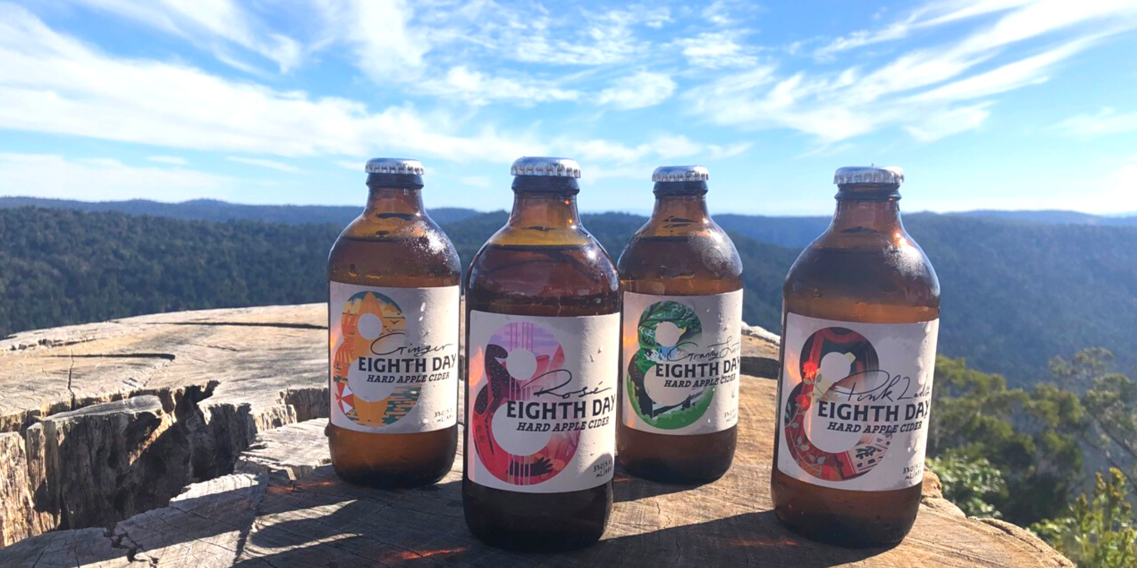 Entire range of Eighth Day Cider sitting on a tree trunk overlooking the view at Binna Burra Lodge