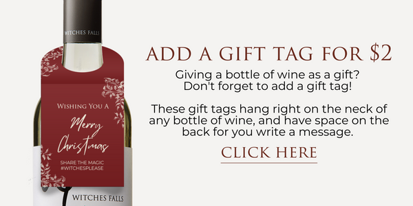 Maroon coloured gift tag hanging from the neck of white wine bottle. Gift Tag reads: Wishing you a merry christmas. Share the Magic #witchesplease