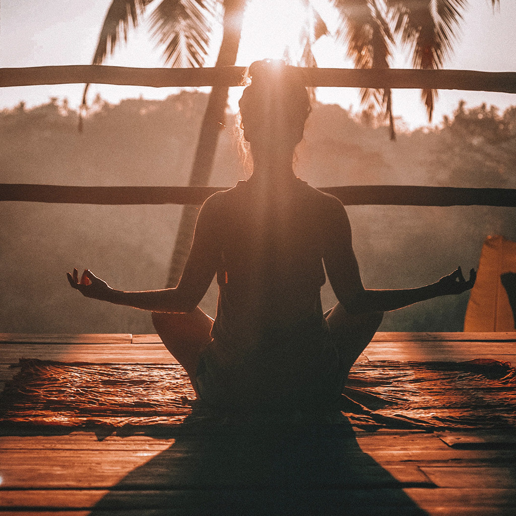 Nainen meditoimassa ilta-auringossa palmun katveessa.