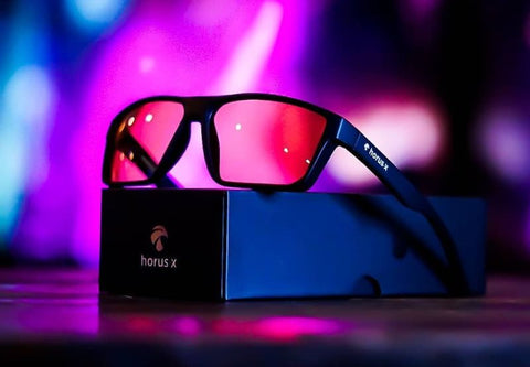 Eine Horus-X-Gaming-Brille wird auf der Verpackung auf einem neonvioletten Hintergrund präsentiert