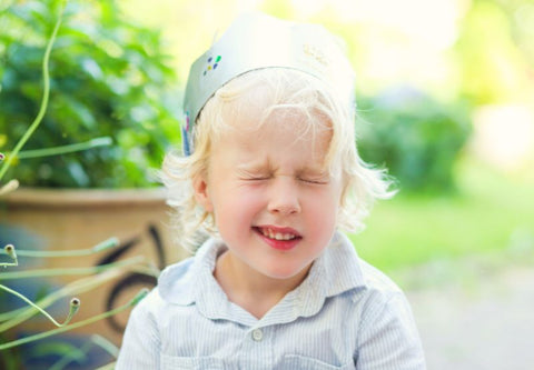 Un enfant blond cligne des yeux sur un fond vert naturel