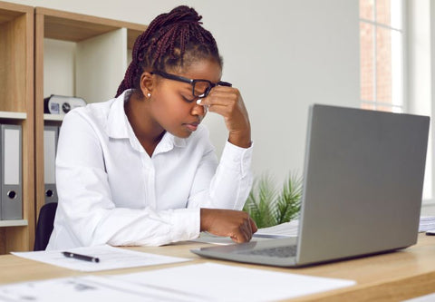 Frau hält ihre Augen vor ihren Laptop