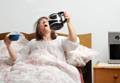 humorvolles Bild einer Frau, die im Schlafanzug im Bett eine Kanne Kaffee trinkt
