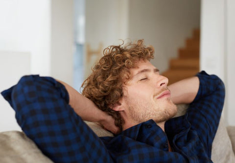 Junger Mann im blauen Hemd auf Sofa mit hinter dem Kopf verschränkten Armen