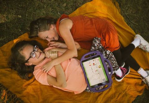 deux enfants jouent sur un canapé autour de leur tablette éducative