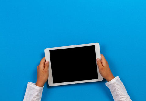 Des mains tiennent un tablette électronique blanche sur fond uni bleu