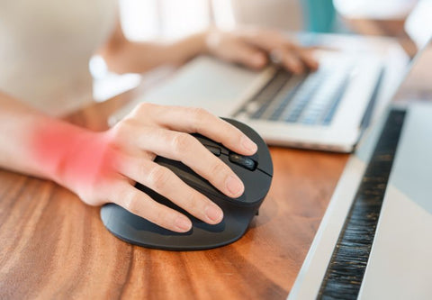 A person suffers from wrist pain in front of their computer