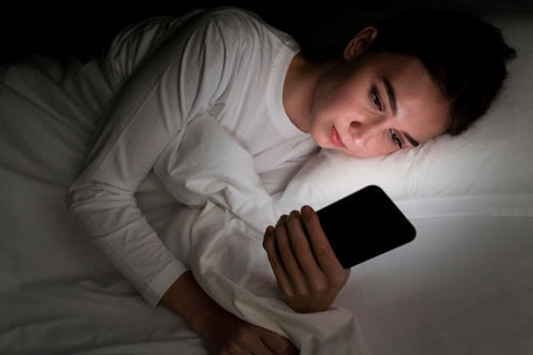 Frau liegt im Bett und blickt in das blaue Licht ihres Telefons