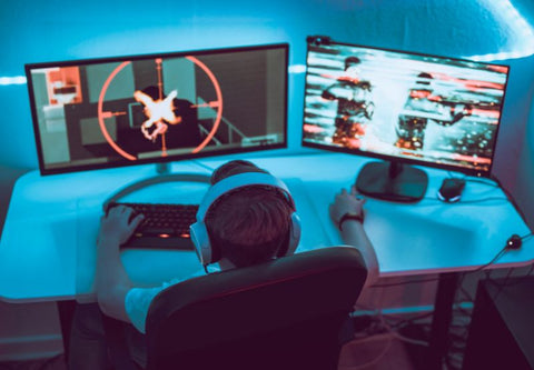 Ein junger Gamer installiert sich vor seinem Gaming-Setup aus zwei Bildschirmen vor einem Hintergrund aus blauem LED-Licht