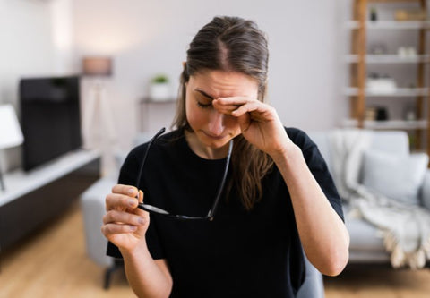 Junge Frau an ihrem Schreibtisch, die sich mit einer Brille in der Hand die Augen reibt