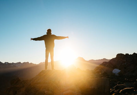 Person auf einem Berg vor einer Landschaft bei Sonnenaufgang