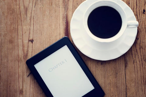 Kindle e-reader on a table next to a cup of coffee