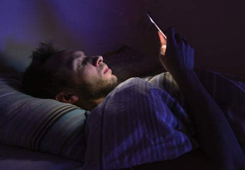 Man lying in bed in the dark lit by the light from his smartphone
