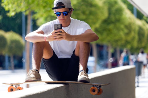 Skateboarder sitzt auf einer niedrigen Mauer und schaut auf sein Telefon