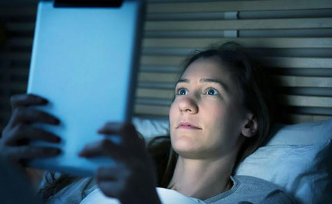 femme dans son lit exposée à la lumière bleue face à un écran de tablette