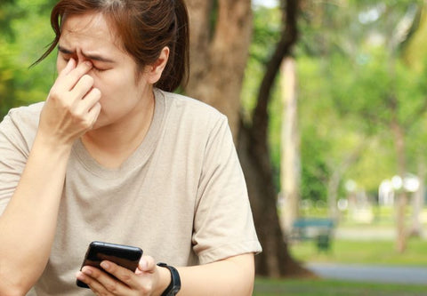 femme se touchant les yeux visiblement en souffrance alors qu'elle tient son téléphone