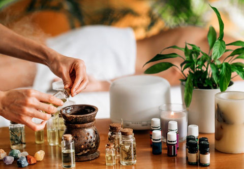 Eine Person bereitet auf ihrem Holztisch, umgeben von Pflanzen, eine Mischung aus ätherischen Ölen zu