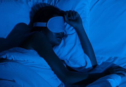 Schlafende Frau mit Schlafmaske im Bett, dunkles Bild