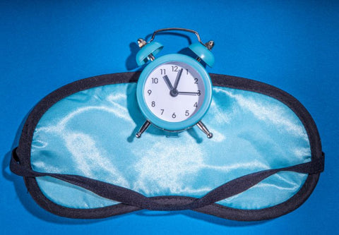 Eine Schlafmaske und ein Wecker auf blauem Hintergrund