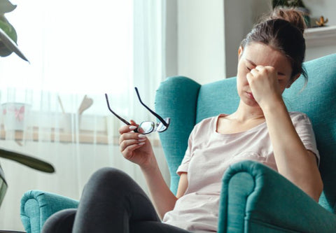 femme fatiguée sur canapé vert bleu qui se tient la tête