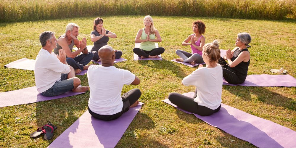 un groupe d'hommes et de femmes d'âge mûr en classe lors d'une retraite de yoga en plein air S