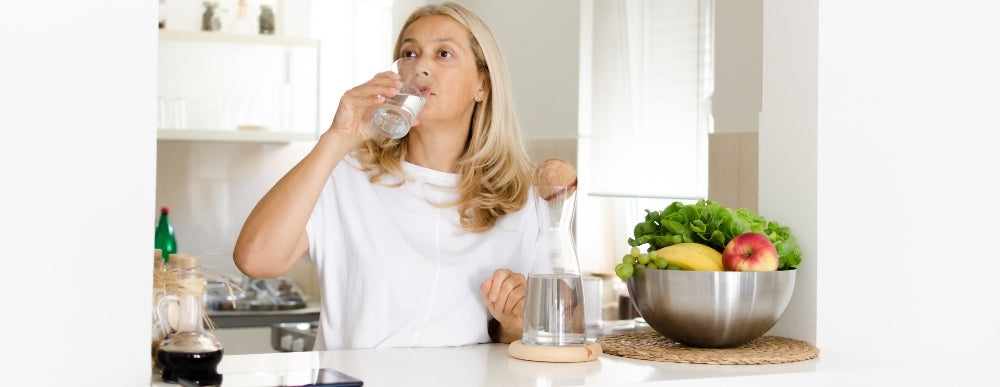 une femme boit de l’eau dans la cuisine.