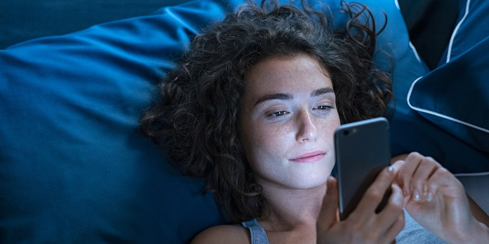 une femme éveillée au lit utilisant un téléphone portable la nuit