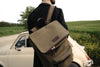 Man with green nubuck leather backpack looks onto rolling green field in front of cream classic car