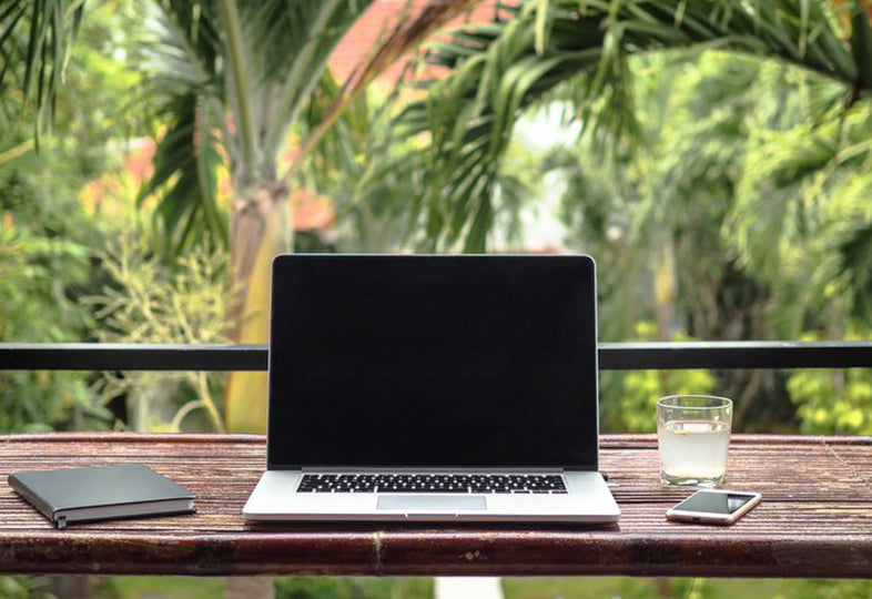 Laptop on wooden desk with view of tropical rainforest