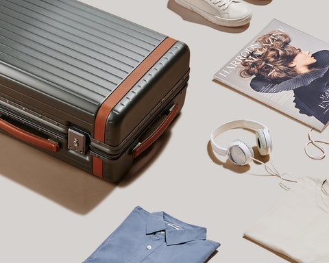 Suitcase, white headphones, folded blue shirt and magazine on cream coloured floor