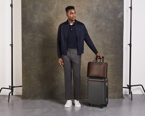 Model standing with a brown leather briefcase and polycarbonate carry-on suitcase