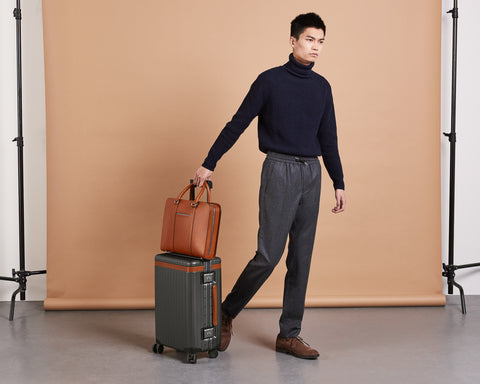 Model walking with a brown leather briefcase and polycarbonate carry-on suitcase